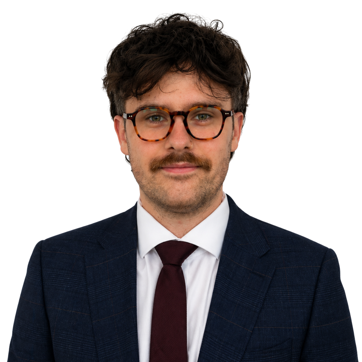 A professional studio headshot of a man with dark curly hair, a mustache, and tortoiseshell glasses. He is wearing a dark blue patterned blazer, a white dress shirt, and a burgundy tie, posed against a plain light grey background.