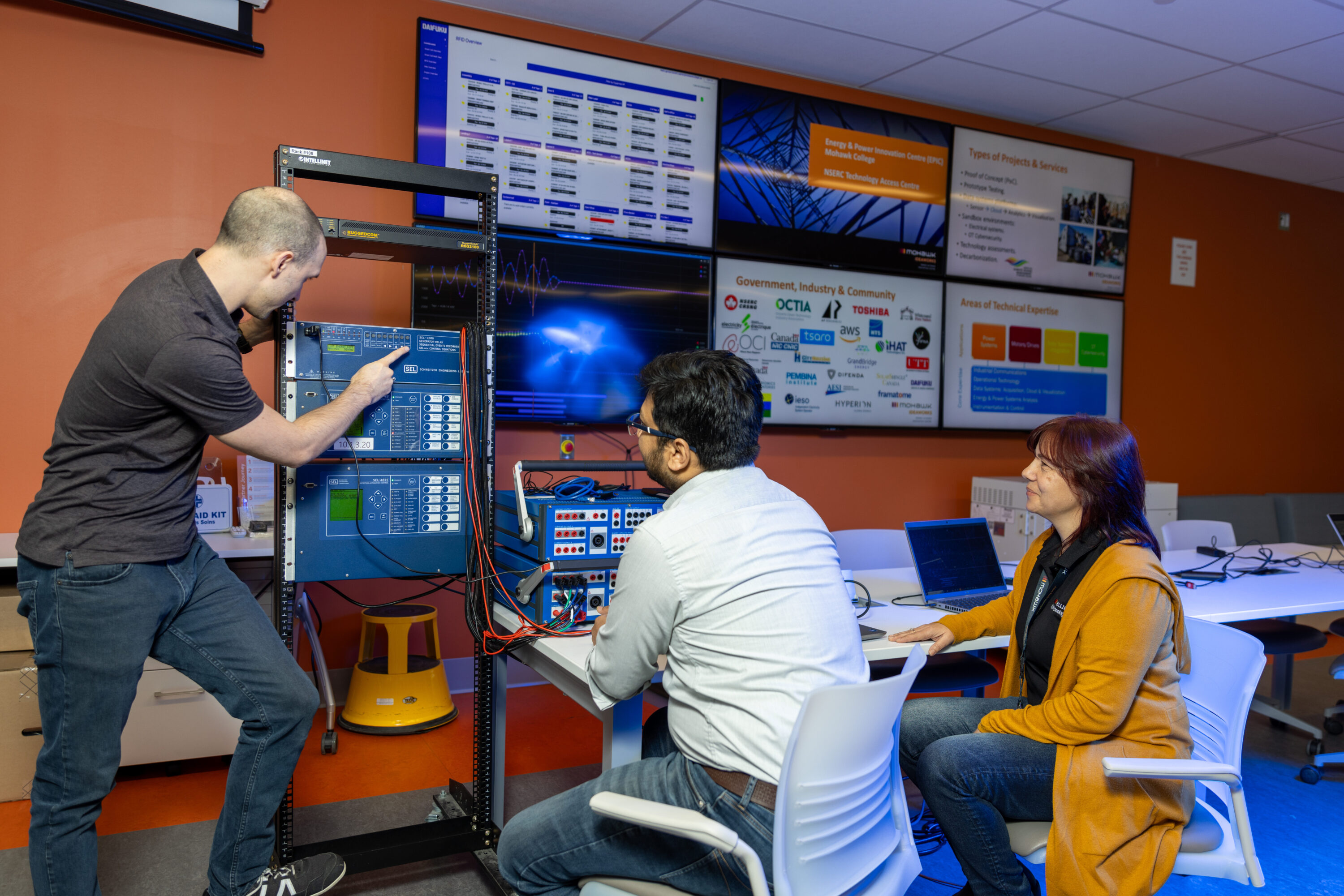 A diverse group of researchers looking at electrical equipment in the EPIC lab in Mohawk College.
